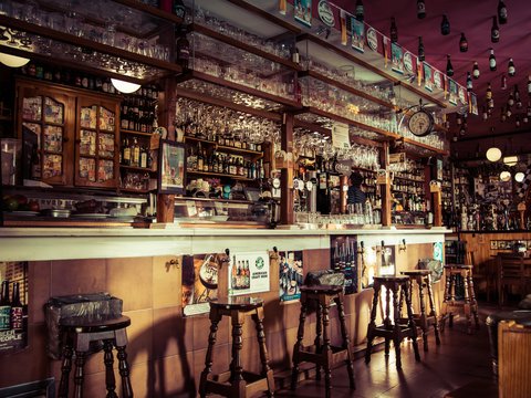 The interior of a bar with stools, glass cups and empty bottles attached to the roof in Madrid