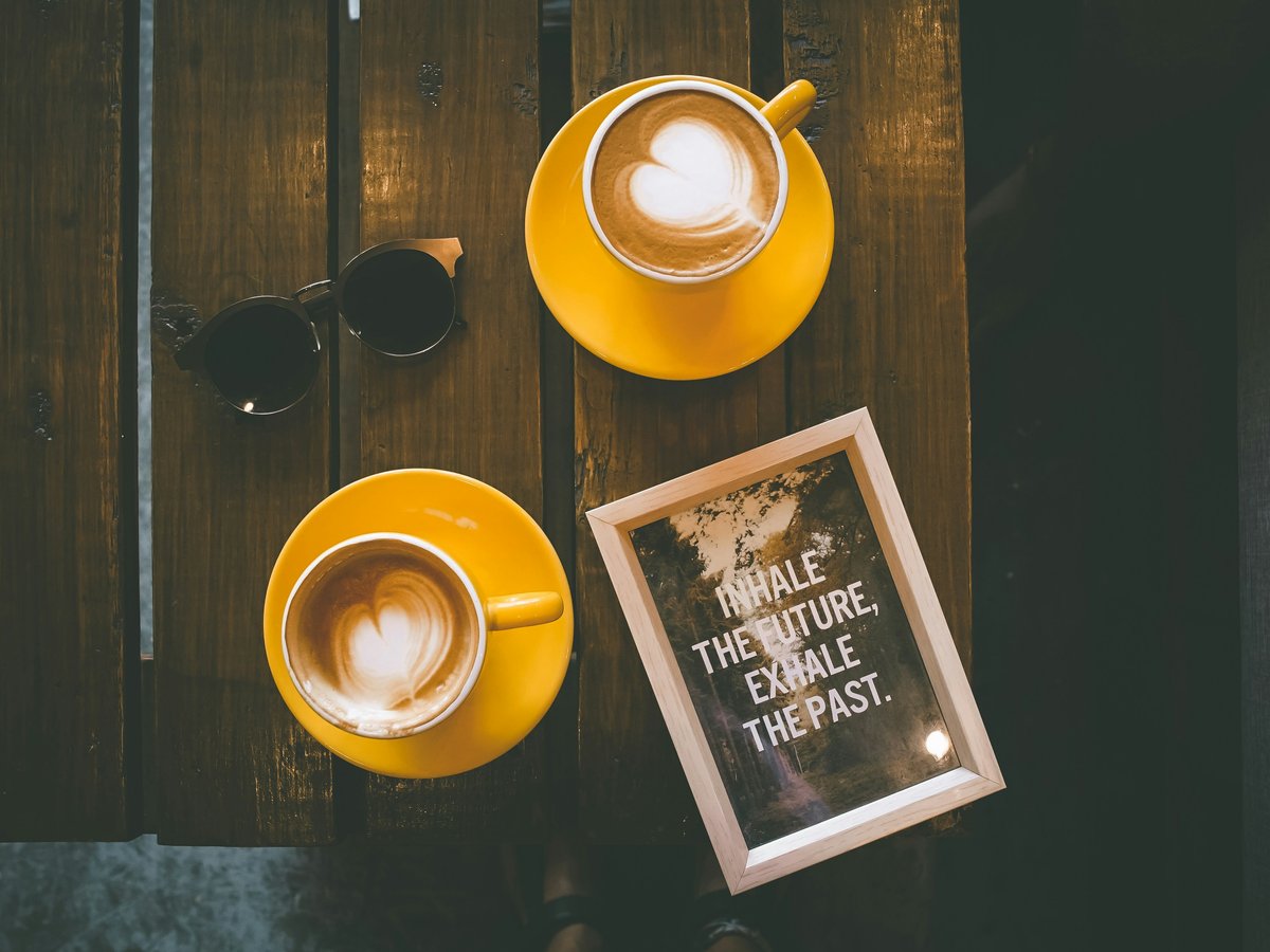 two coffee lattes in yellow cup with saucer on brown wooden table