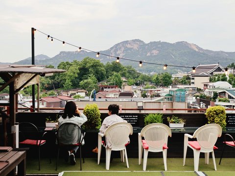 Two people sitting on a rooftop overlooking a city.