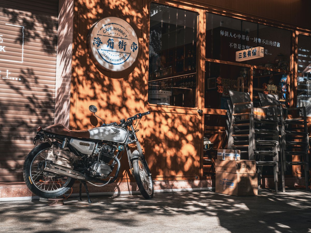 Motorcycle parked outside a cafe with chairs stacked chairs