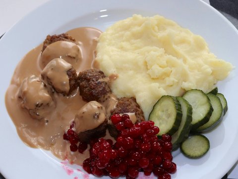 a white plate topped with meatballs, mashed potatoes and cucumbers
