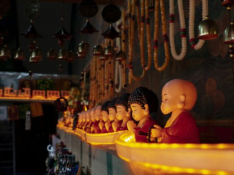 A row of small monk figurines with prayer beads in a dimly lit temple
