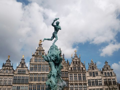 A bronze statue stands atop a fountain with buildings behind.