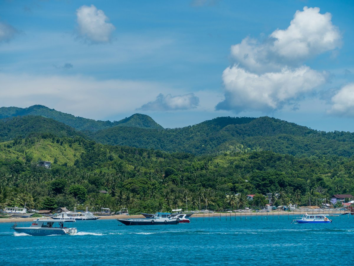 white boat on sea near green mountain under white clouds and blue sky during daytime