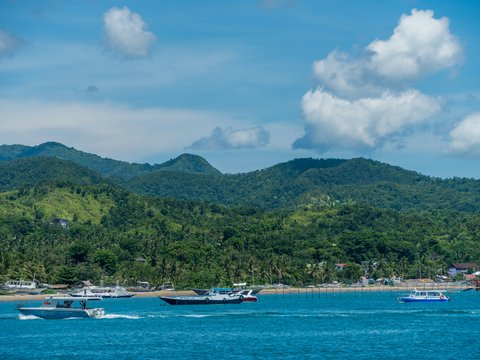 white boat on sea near green mountain under white clouds and blue sky during daytime