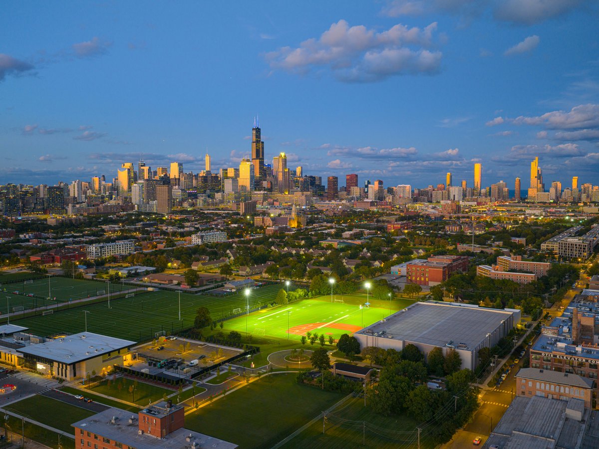 City skyline at dusk with illuminated baseball fields.