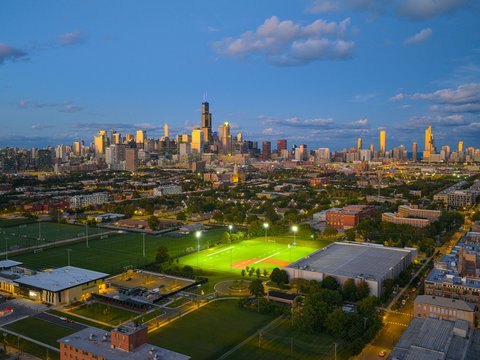 City skyline at dusk with illuminated baseball fields.