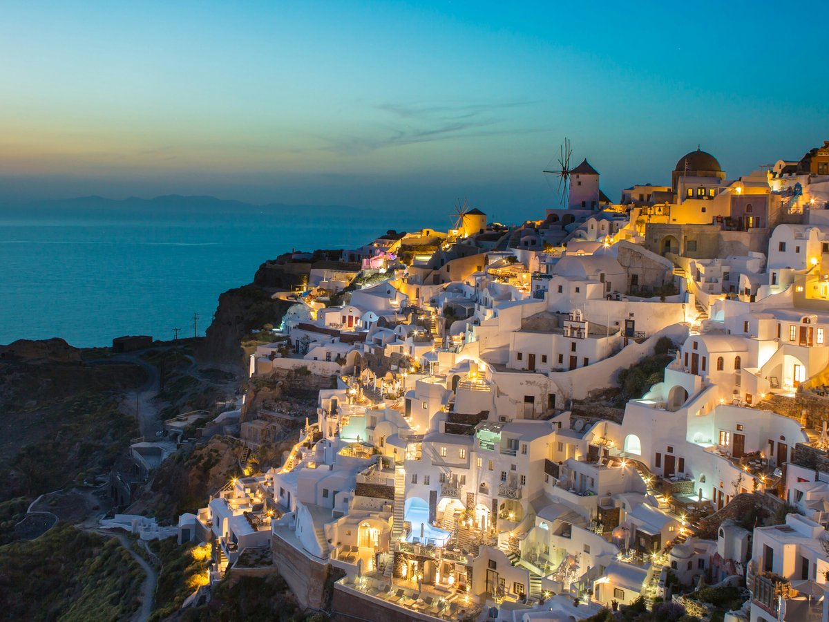 White buildings on a cliffside in Oia, Greece, illuminated by warm evening light