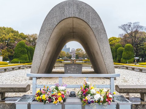 a large stone structure with flowers in front of it with Hiroshima Peace Memorial in the background