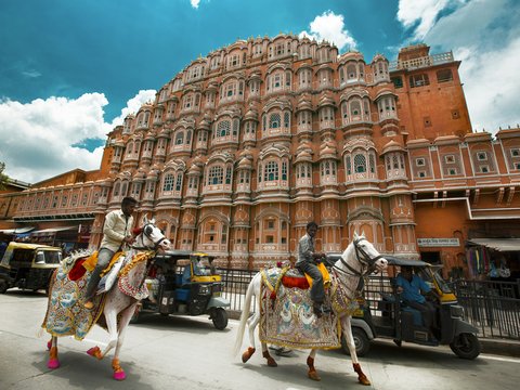 Two men riding decorated white horses past Hawa Mahal in Jaipur