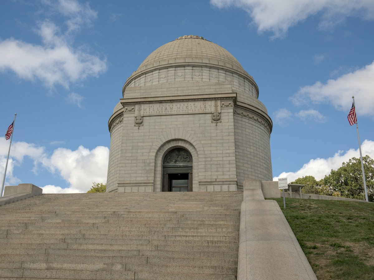 Stone monument with dome and flags under blue sky.