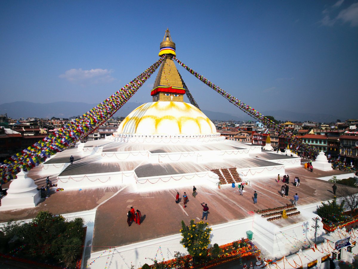 A large white stupa with prayer flags and buildings.