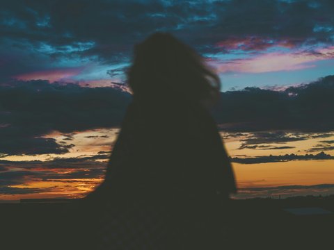 silhouette of woman sitting on beach during sunset