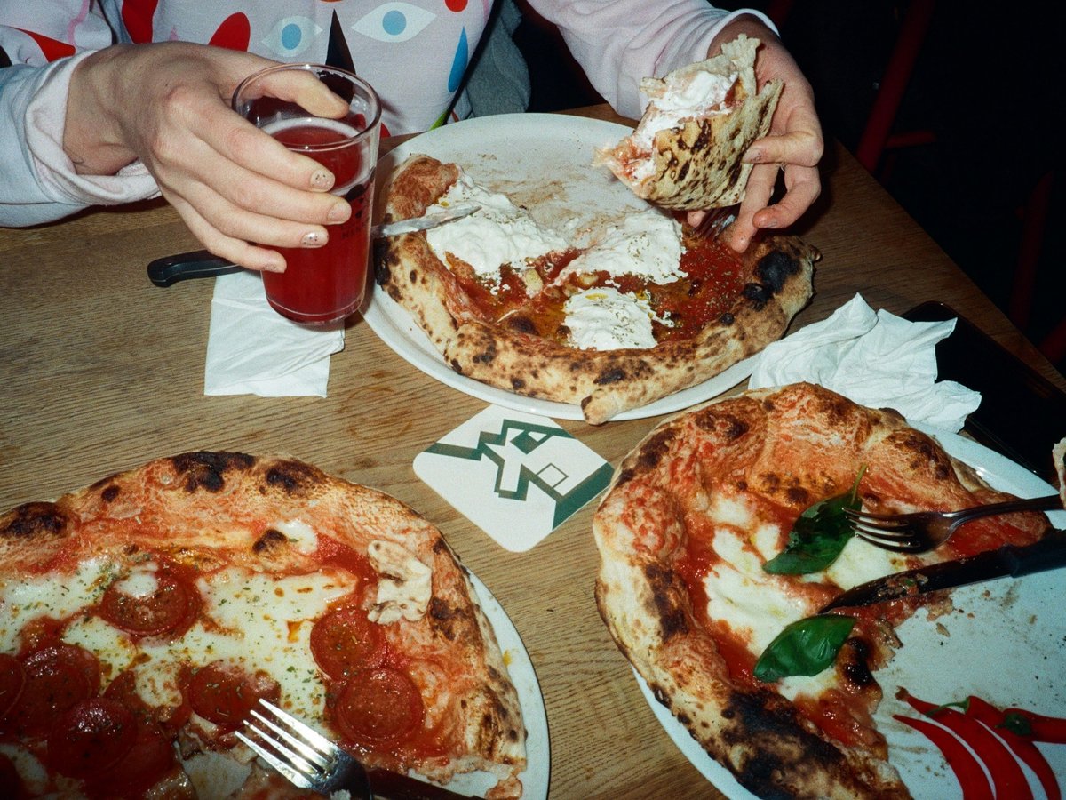 Three pizzas and a drink on a wooden table.