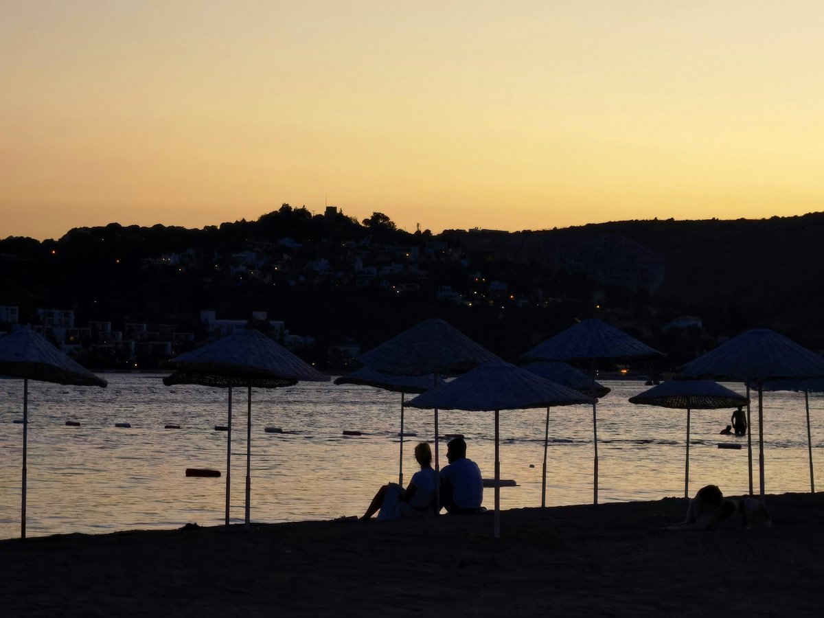 silhouette of people sitting on bench near body of water during sunset