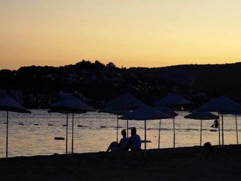 silhouette of people sitting on bench near body of water during sunset