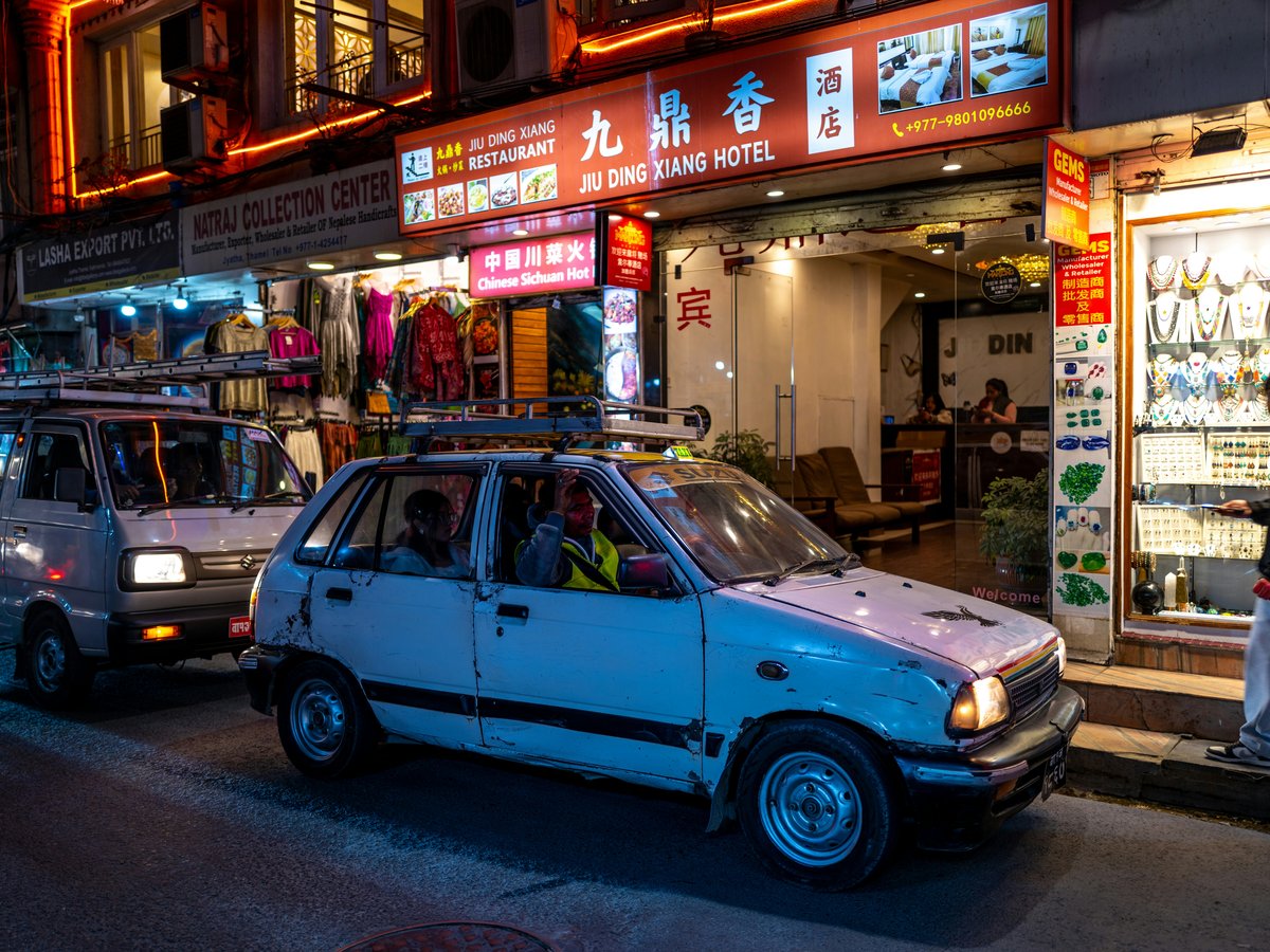 Cars on a street at night with glowing signs.