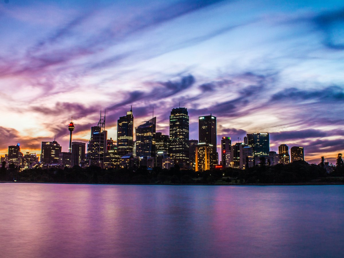 lighted city buildings near body of water under cloudy sky