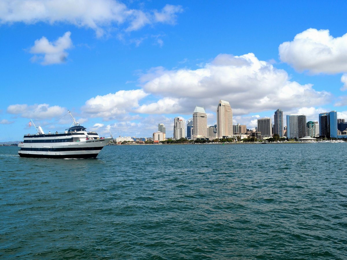 white and black boat on sea near city buildings under blue and white sunny cloudy sky
