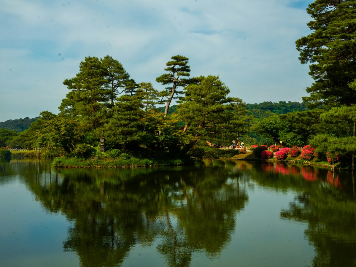 Lush trees reflect in a pond with a red bridge