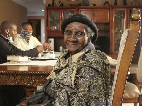 an old woman sitting at a table with two men in the background