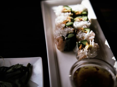 a white plate topped with sushi next to a bowl of sauce