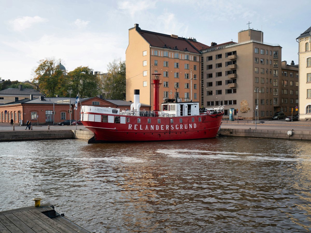 a large red boat traveling down a river next to tall buildings