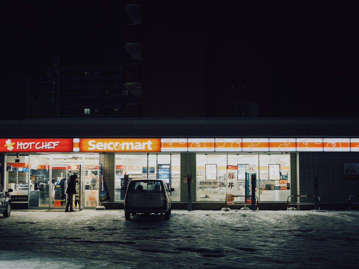 Convenience store at night with cars parked outside.