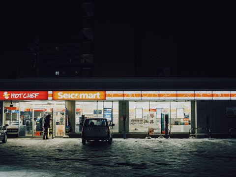 Convenience store at night with cars parked outside.
