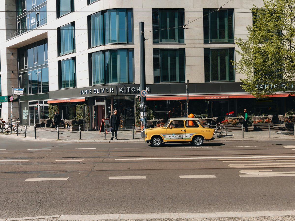 Yellow taxi drives past a modern building on street.