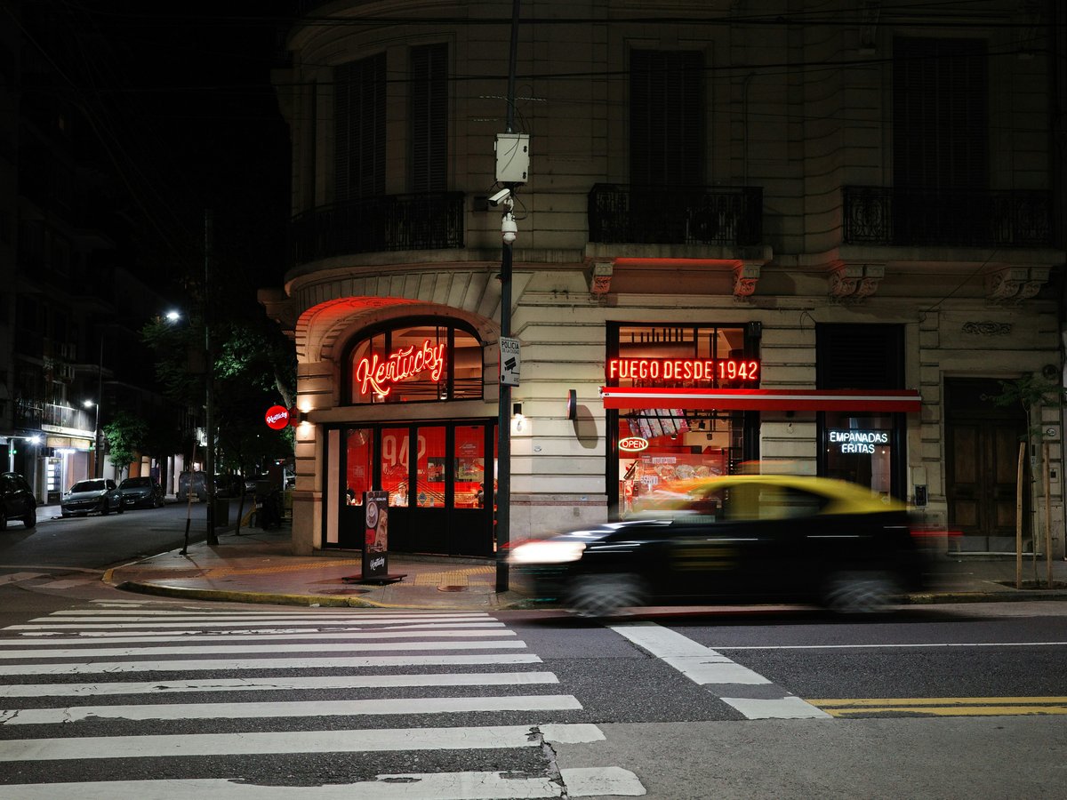 A taxi drives past a brightly lit building at night.