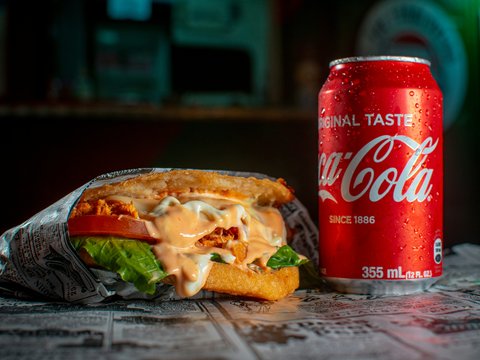 a can of soda and a sandwich on a table