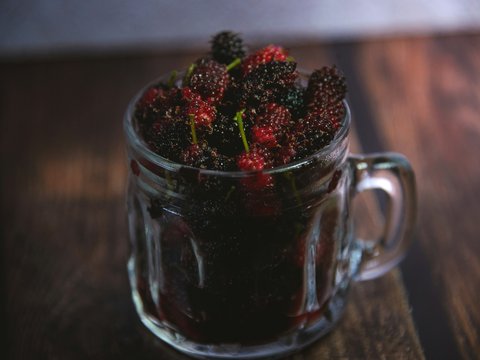 a glass mug filled with raspberries on top of a wooden table