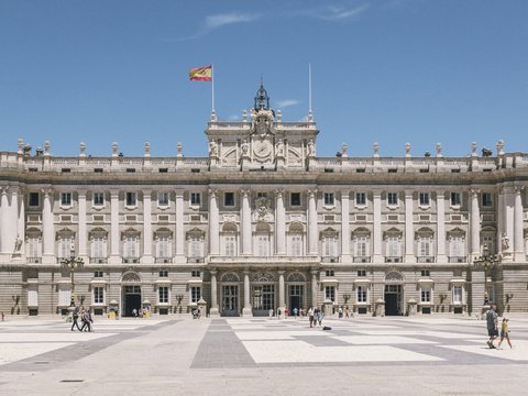 a large building with columns and a flag on top with Royal Palace of Madrid in the background