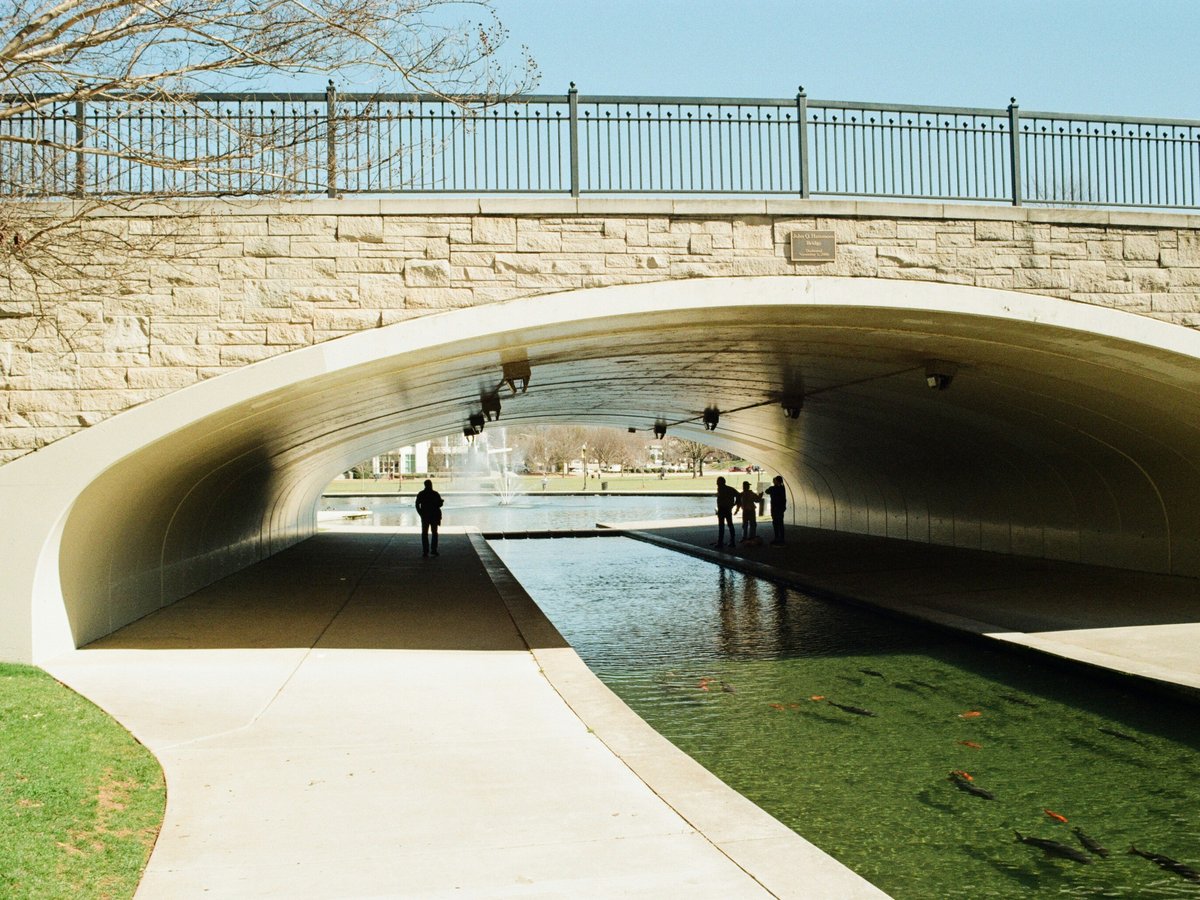 People walk along a canal under a stone bridge.