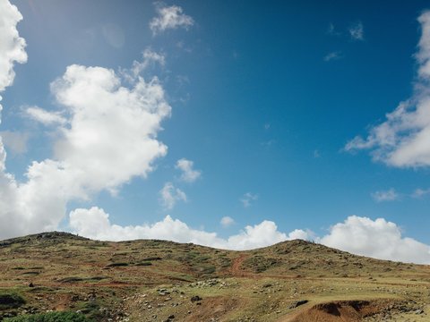 a dirt road going up a hill under a cloudy blue sky