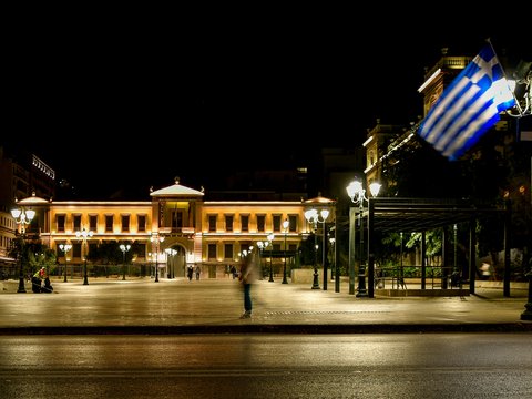 Grand building illuminated at night with a waving greek flag.