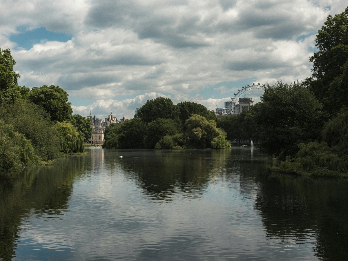 A peaceful park with a lake under cloudy skies.