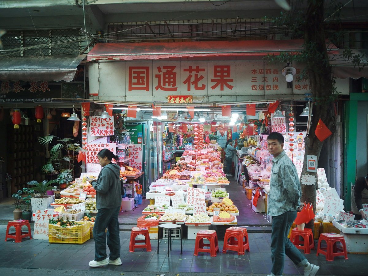 People walk past a busy fruit and flower market stall