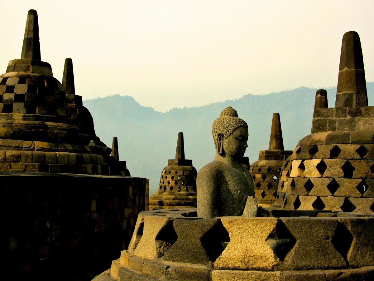 A stone Buddha statue among bell-shaped stupas at Borobudur temple in Indonesia
