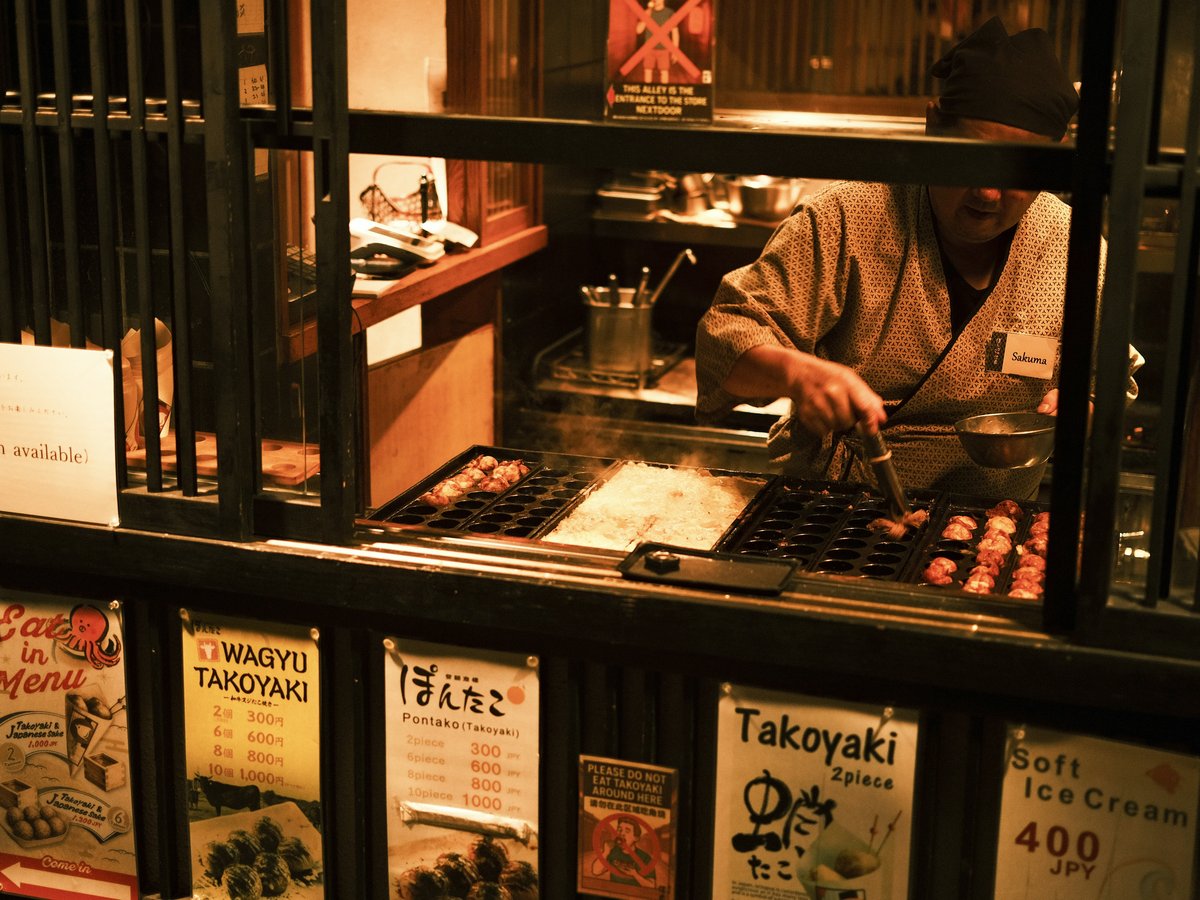 Chef preparing takoyaki at a street food stall.