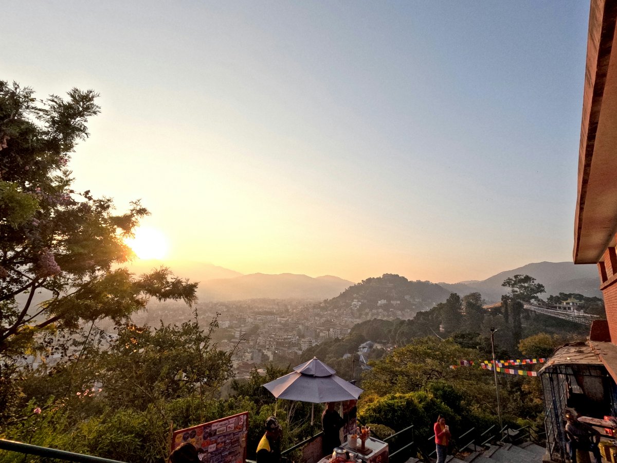 Sunset over a hilly city with trees in foreground.
