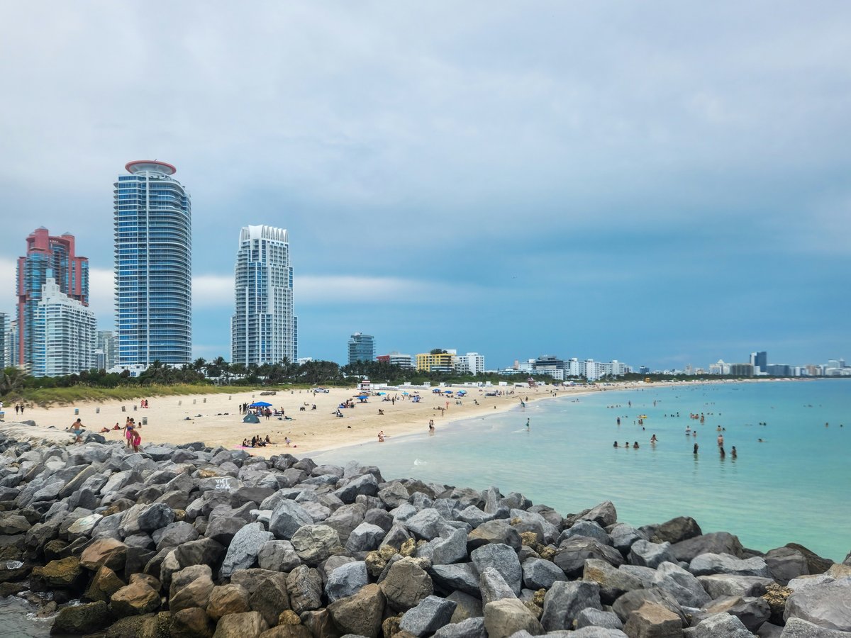 A view of a beach with people in the water and skyscrapers in the background