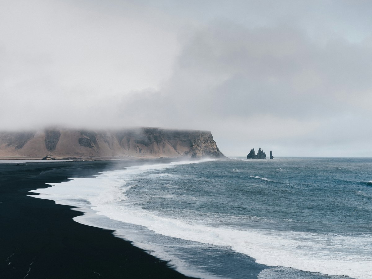 black sand near body of water under the cloudy sky during daytime