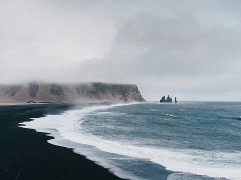black sand near body of water under the cloudy sky during daytime