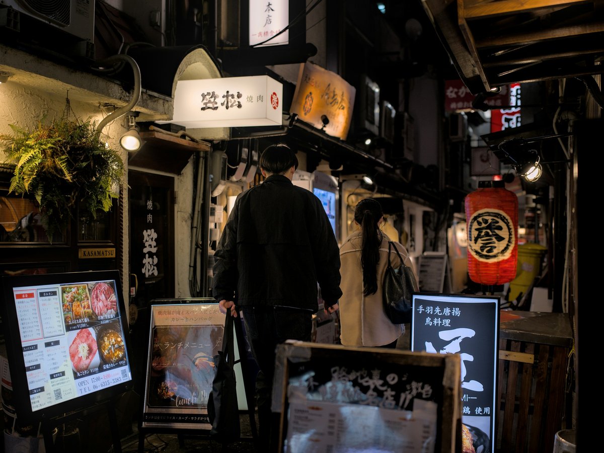 People walk down a narrow, illuminated japanese street.