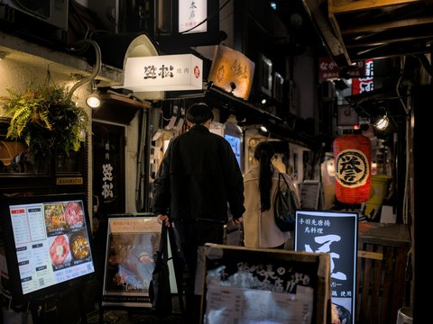 People walk down a narrow, illuminated japanese street.