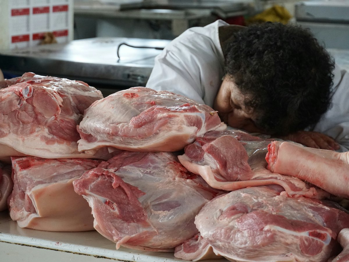 Butcher rests head on pile of raw pork cuts