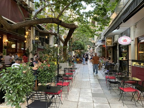 a group of people walking down a sidewalk next to tables and chairs