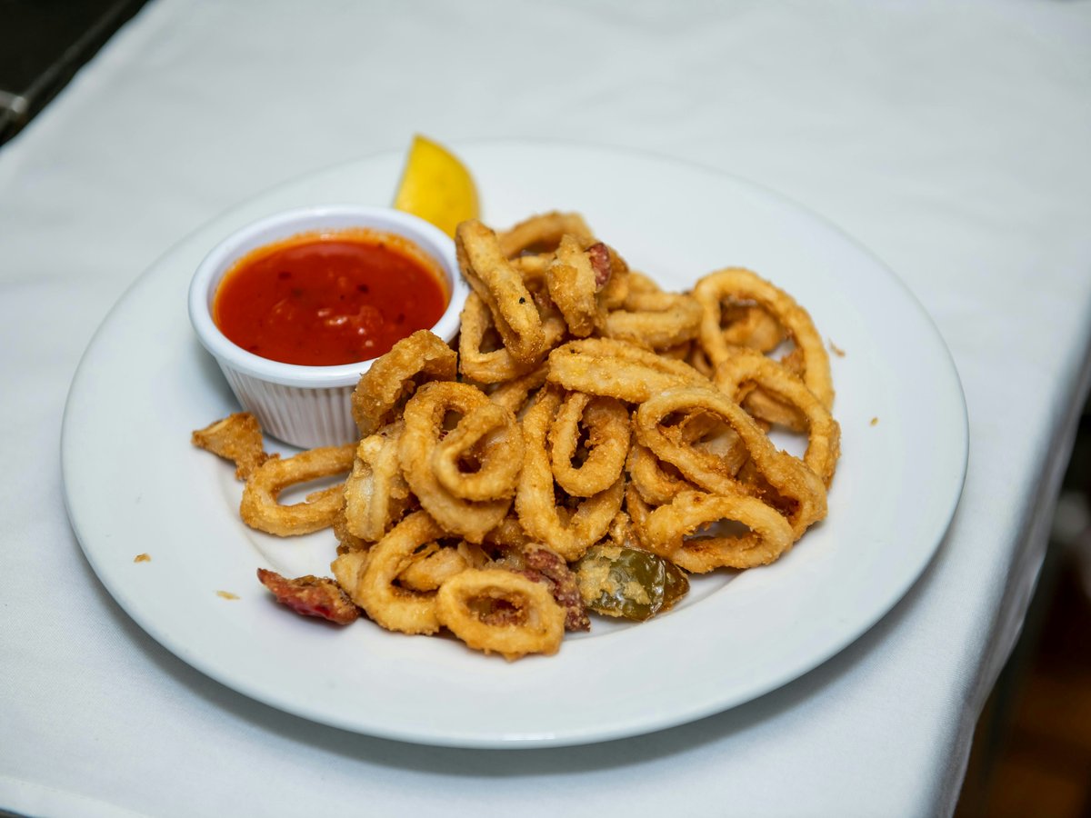 A plate of onion rings with ketchup and a lemon wedge